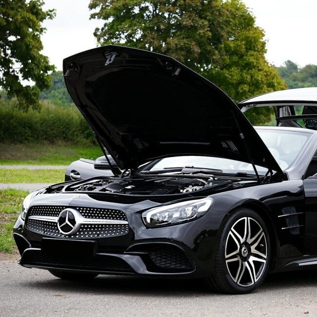 Sleek black convertible car with hood open on a scenic outdoor road.